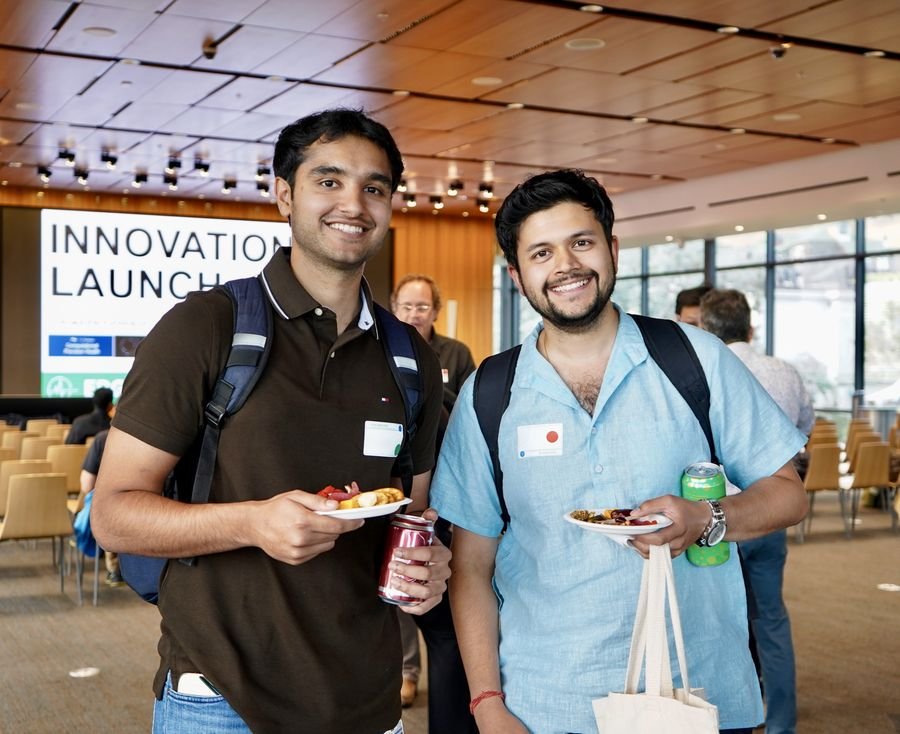 Two smiling attendees holding plates of food in front of the Innovation Launch slide