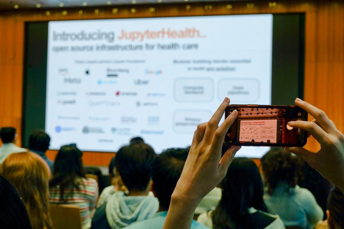 An attendee photographing the &ldquo;Introducing JupyterHealth: open source infrastructure for health care&rdquo; slide on a phone