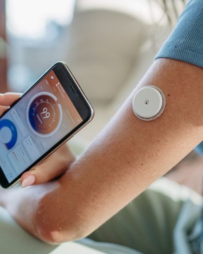 Continuous glucose monitor sensor on an arm next to a phone showing health data