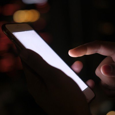 Close-up of a hand tapping a smartphone screen lit up in the dark